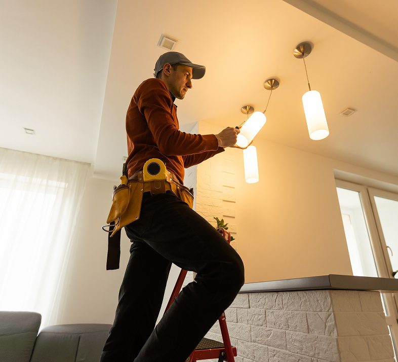 Electrician fixing ceiling light on ladder.